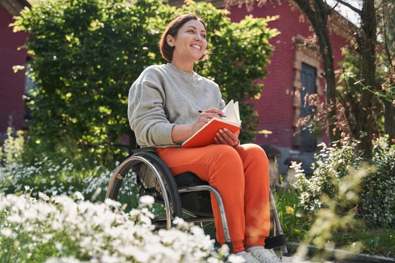 Happy disabled woman in wheelchair smiling and writing in journal